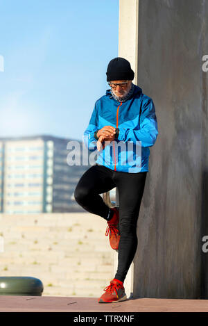 Senior Uomo con cuffie guardando orologio da polso mentre ti alleni Foto Stock