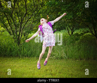 Allegro ragazza con zaino saltando su campo erboso a park Foto Stock