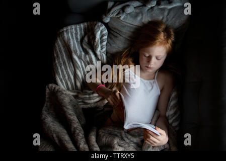 Poco Redhead ragazza distesa verso il basso la lettura di un libro Foto Stock