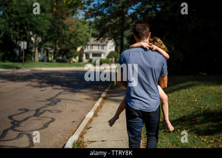 Vista posteriore del padre che porta la figlia mentre si cammina sul sentiero Foto Stock