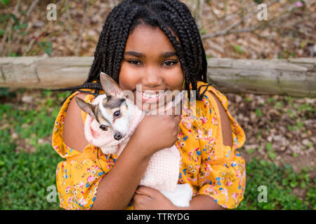 Ritratto di ragazza sorridente che trasportano carino Chihuahua rimanendo in posizione di parcheggio Foto Stock