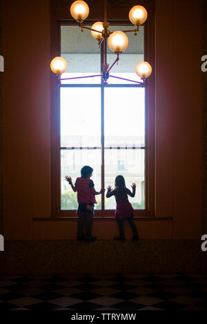 Silhouette di due bambini che guardano da una finestra di grandi dimensioni Foto Stock