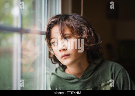 Un ragazzo sguardi fuori una finestra con espressione seria sul suo volto Foto Stock