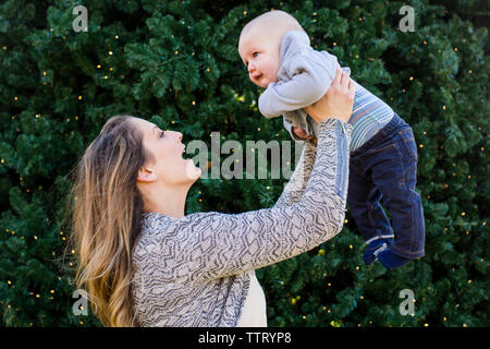 Un sorridente madre teneramente solleva la sua baby boy in aria Foto Stock