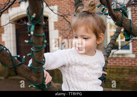 Un simpatico bambina si siede in una struttura ad albero di un parco Foto Stock