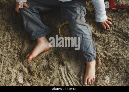 La metà inferiore di un piccolo ragazzo giocando a piedi nudi in una sandbox Foto Stock