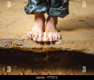 Sezione bassa di un piccolo bambino di piedi sporchi sul coperto di sabbia cengia rocciosa Foto Stock