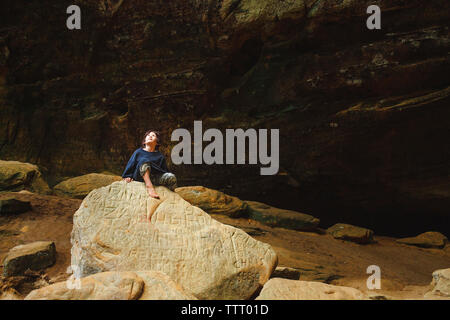 Un piccolo ragazzo si siede a piedi nudi su una roccia d'oro circondato da pareti di roccia Foto Stock