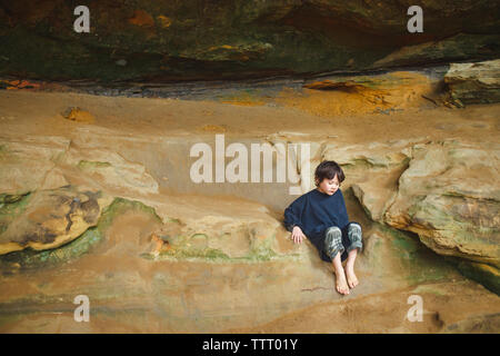 Un bambino piccolo si siede a piedi nudi cullati sulla rocciosa battuta di arenaria nella gola Foto Stock