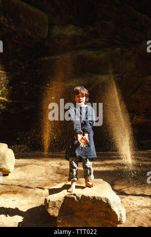 Un piccolo bambino a piedi nudi getta sabbia dorata in aria in gola soleggiato Foto Stock