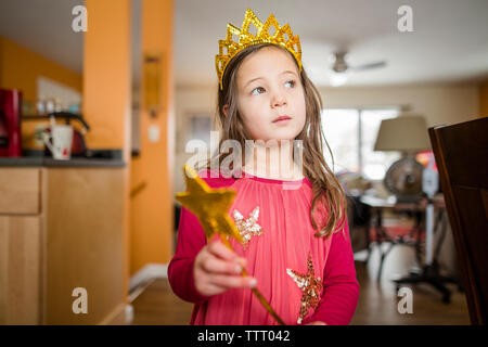 Una bambina con un espressione seria indossa una corona e fiabesco wand Foto Stock