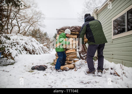 Un piccolo ragazzo aiuta il suo padre raccolgono la legna da una pila di legno nella neve Foto Stock