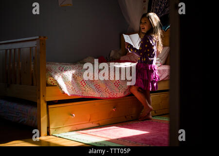 Ritratto di un felice bambina la lettura di un libro da sola nella sua camera da letto Foto Stock