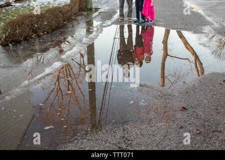 Una famiglia sta insieme si riflette in una grande pozza sulla strada Foto Stock