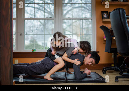 Un padre detiene una posizione di yoga con due bambini accatastati sul suo retro Foto Stock