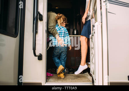 Madre abbracciando la figlia mentre in piedi con il marito in camper Foto Stock