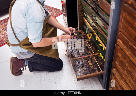 Sezione bassa dell'uomo disponendo gli alfabeti di legno nel cassetto di stampa Foto Stock