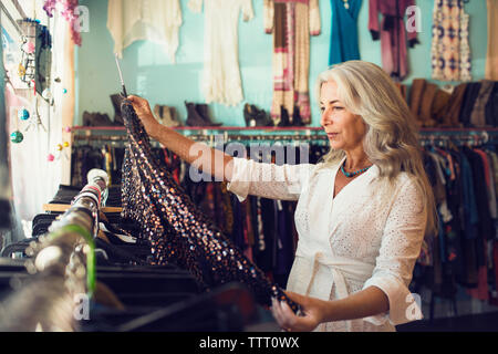 Femmina matura proprietario esaminando abito in negozio di abbigliamento Foto Stock