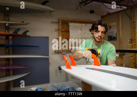 lavoratore che regola le alette sulla tavola da surf in officina Foto Stock