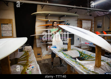 lavoratore che esamina la tavola da surf in officina Foto Stock