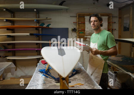 Lavoratore di sesso maschile con la tavola da surf di controllo in officina Foto Stock