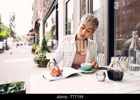 Donna iscritto in agenda a sidewalk cafe Foto Stock