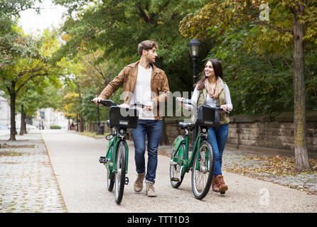 Paio di parlare mentre si cammina con la bicicletta su strada in posizione di parcheggio Foto Stock