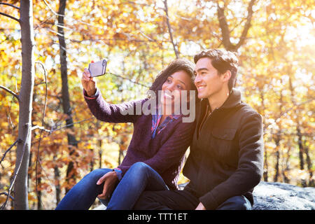 Donna prendendo selfie mentre è seduto con il mio ragazzo su roccia nella foresta Foto Stock