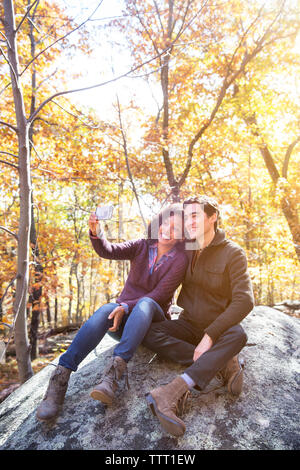 Giovane tenendo selfie seduti sulla roccia nella foresta Foto Stock