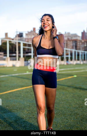 Felice atleta femminile parlare tramite cuffie mentre camminando sul campo erboso Foto Stock