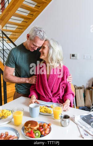 Giovane romancing mentre in piedi dal tavolo da pranzo a casa Foto Stock