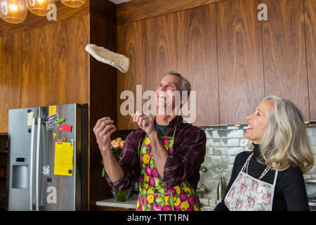 Allegro uomo tossing pasta della pizza durante la preparazione di alimenti da donna in cucina a casa Foto Stock