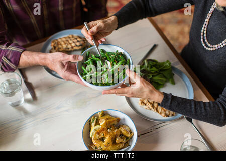 Sezione mediana dell'uomo dando una ciotola di fagiolini cotti alla donna al tavolo da pranzo Foto Stock