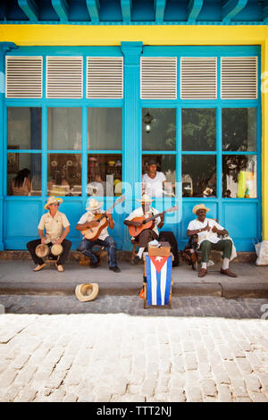 Gli uomini che giocano la musica mentre è seduto sul marciapiede Foto Stock