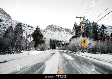 Paese strada che conduce verso le montagne in inverno contro il cielo chiaro Foto Stock