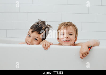 I fratelli tenendo bolla bagno in vasca bianca con un sorriso Foto Stock