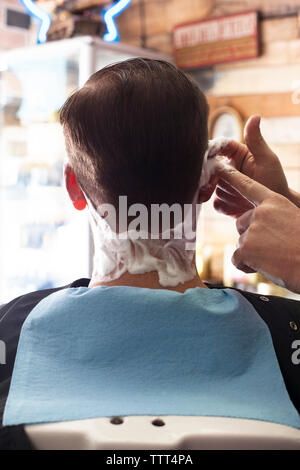 Immagine ritagliata del barbiere di applicare la crema per la rasatura con il cliente Foto Stock