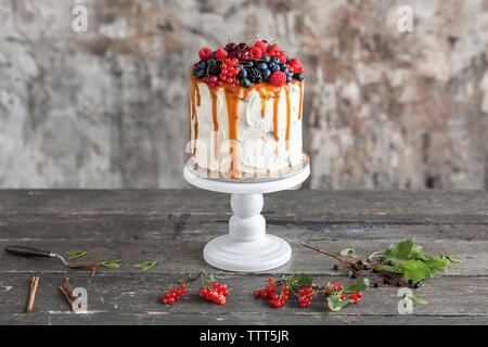 Close-up di torta con caramello e bacche sul tavolo di legno contro la parete arrugginito a casa Foto Stock