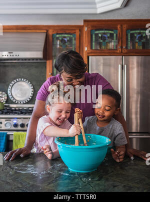 Madre supervisionare i bambini mentre essi mescolare ingredienti insieme Foto Stock