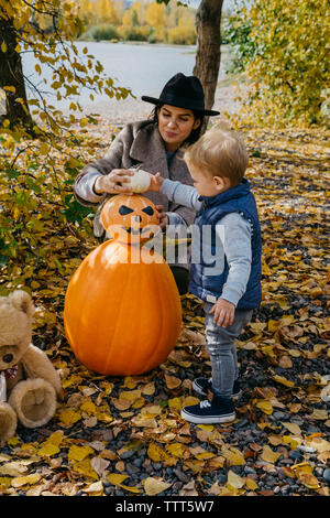 Madre e figlio carino decorare jack o lanterna nel parco durante l'autunno Foto Stock