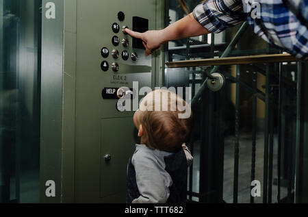 Figlio guardando la madre premendo il pulsante di ascensore Foto Stock