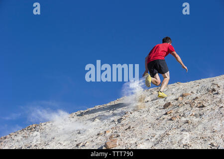 Basso angolo di visione dell'uomo jogging sulla montagna contro il cielo blu chiaro Foto Stock