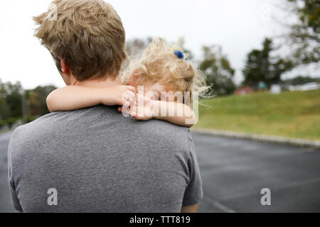 Vista posteriore del padre che porta la figlia a pelo su strada Foto Stock