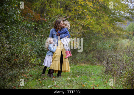 Madre di due bambini in piedi insieme baciare bambino sulla guancia Foto Stock