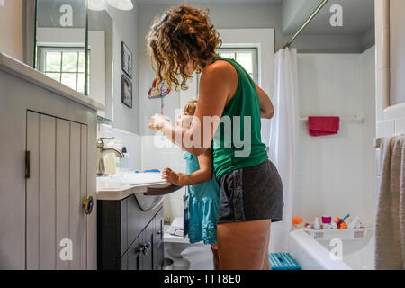 Mom toddler di spazzolamento dei denti figlie in bagno bianco Foto Stock