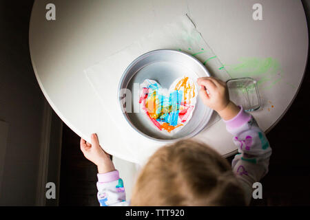 Angolo di Alta Vista della ragazza la colorazione di forma di cuore la carta nel contenitore sul tavolo Foto Stock