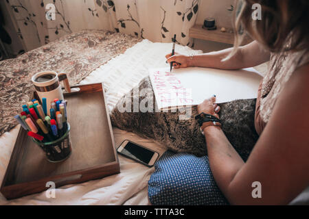 Immagine ritagliata dell'artista Fare calligrafia mentre è seduto sul letto di casa Foto Stock