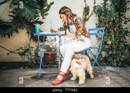 Per tutta la lunghezza della pittura dell'artista mentre è seduto da cane sulla sedia in cortile Foto Stock