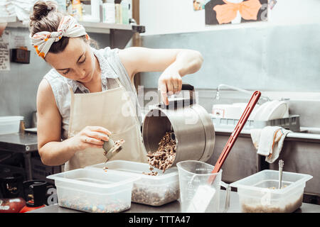 Donna macinato versare gli ingredienti nel contenitore mentre la fabbricazione di gelato in cucina commerciale Foto Stock