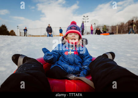 Sezione bassa di madre in figlia slittino sulla neve campo coperto contro il cielo nuvoloso Foto Stock